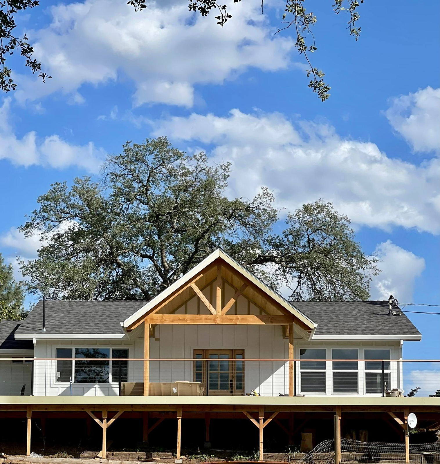 Completed Lane Built custom home with white board and batten siding, a heavy timber gable porch and a covered deck
